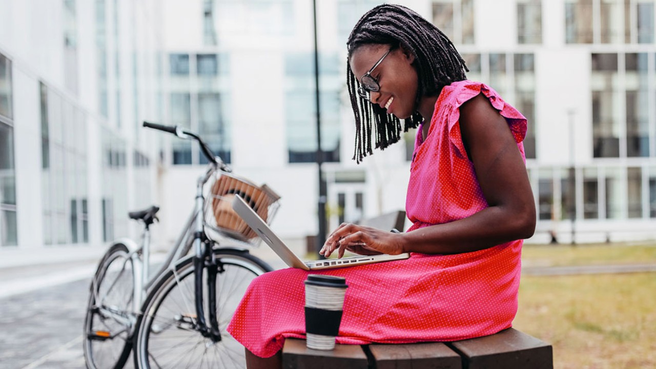 Young woman working on laptop while sitting on bench in campus
