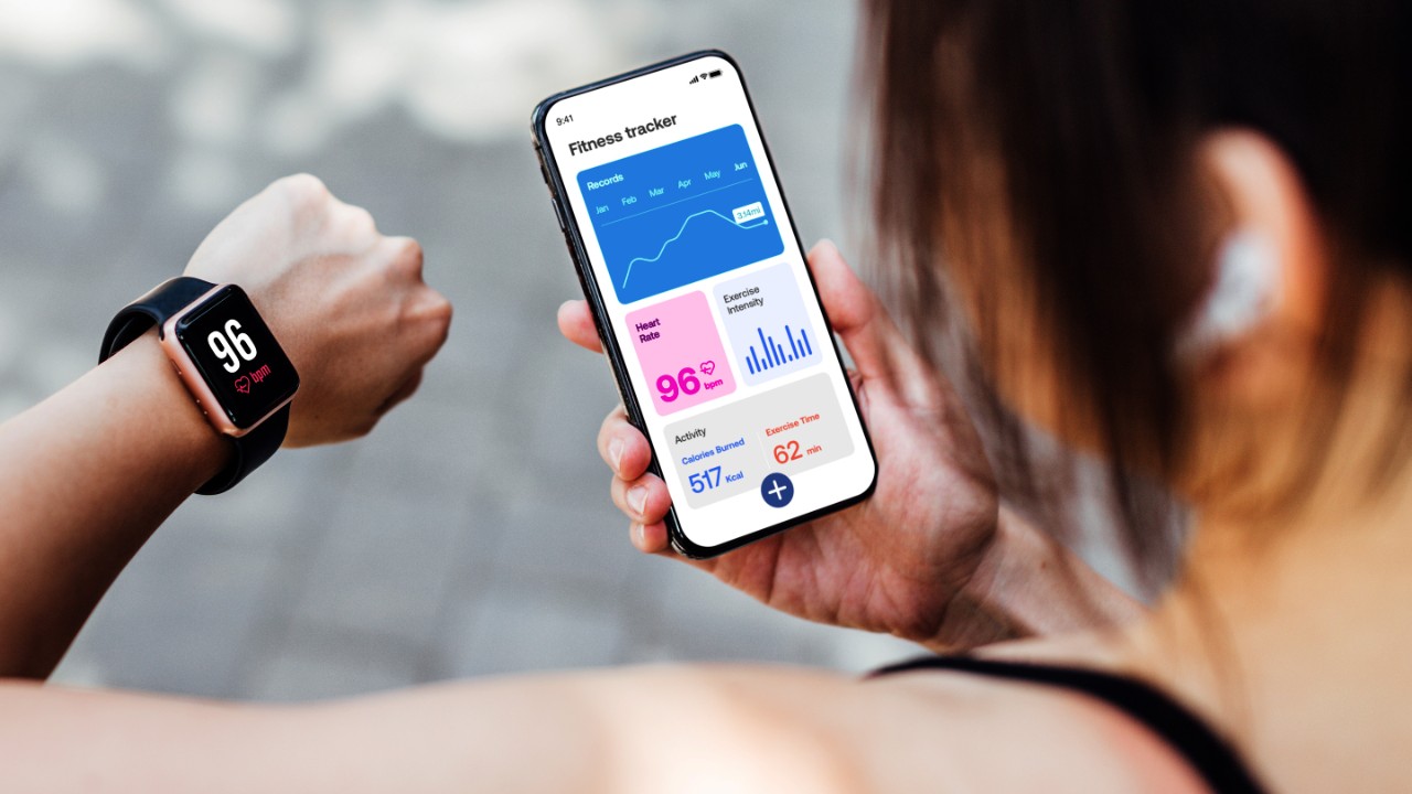 Young Woman Using Fitness Tracker App On Smart Watch And Smartphone